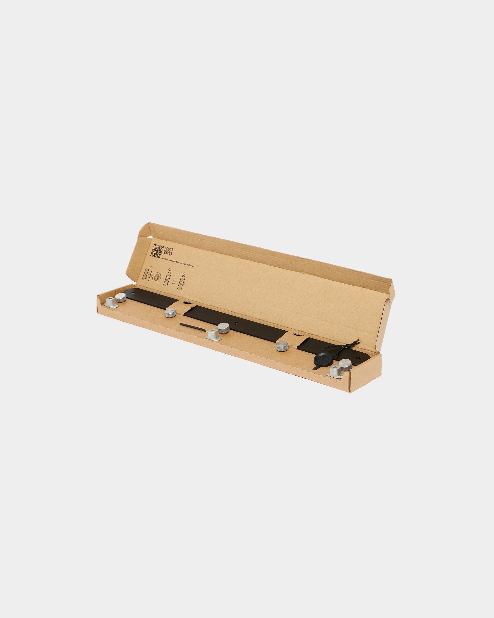 An open long, slim cardboard box containing organized metal components and precision tools for installing WoodUpp acoustic panels or accessories.